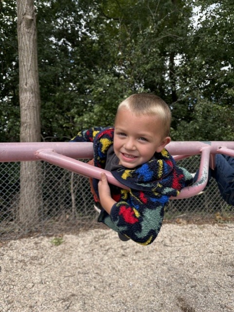 A smiling boy leans on the playground climbing bars during outdoor recess